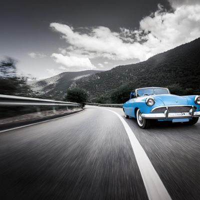 Firefly blue fifties car driving fast on the black and white winding road in mountains; extreme fish.jpg