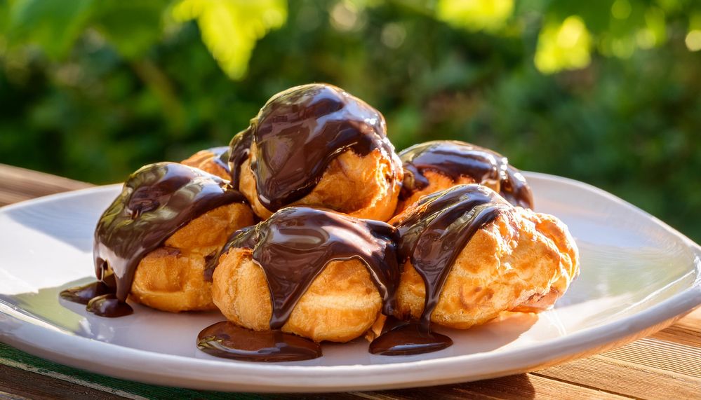 Firefly profiteroles covered with chocolate sauce on a white plate on a terrace in a green garden in.jpg